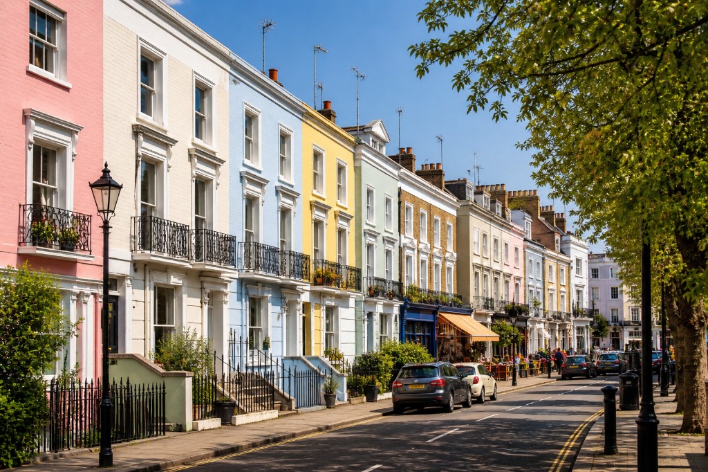 Pastel-painted Victorian terraces on a sunlit Notting Hill street: sash windows, iron railings and tree-lined road